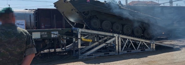 Tracked armoured vehicle rolling from a rail car down the ramp